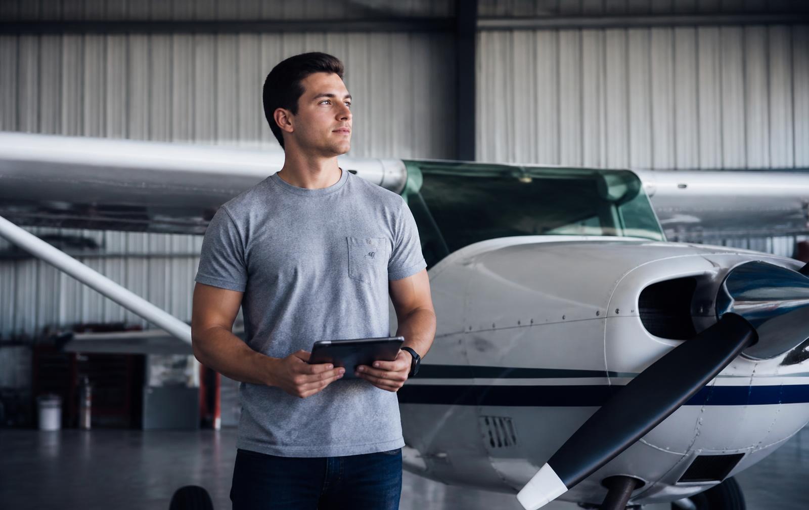 Pilot with a tablet standing beside a single-engine aircraft in a hangar