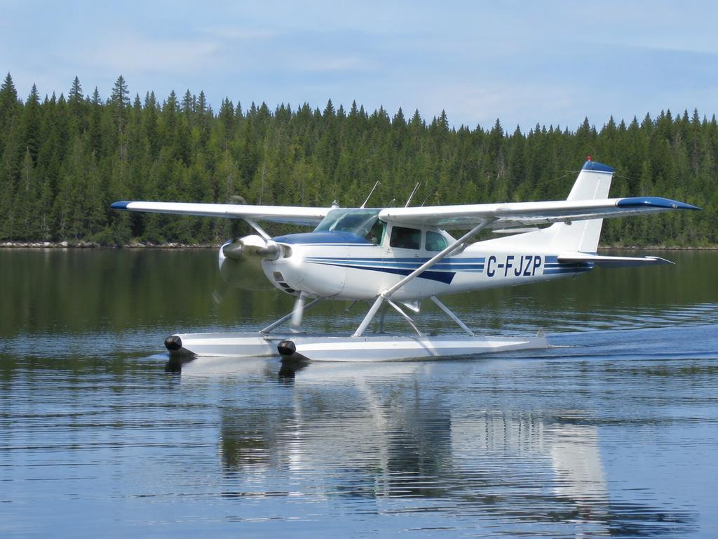 Floatplane taxiing on a calm lake surrounded by pine forest